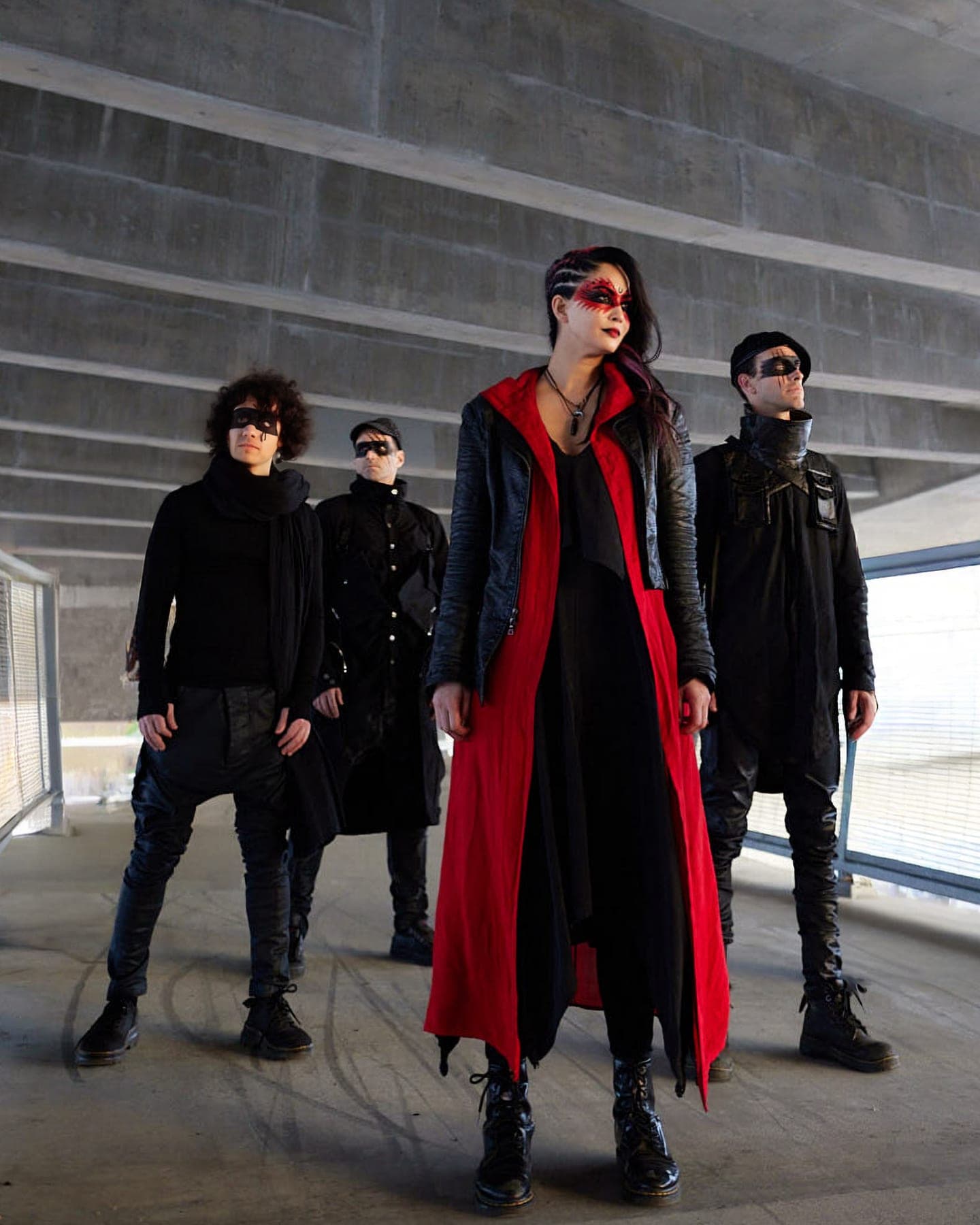 AL1CE in masks and a red floor-length coat beneath a concrete overpass